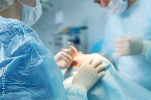 Male surgeon and assistant performing facilift operation (unrecognizable patient). Selective focus. photo