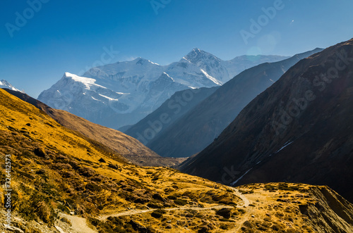 Trekking route from Manang village to Torung La against snow covered Mt. Gangapurna summit in sunny day. Annapurna circuit trek, Nepal. photo