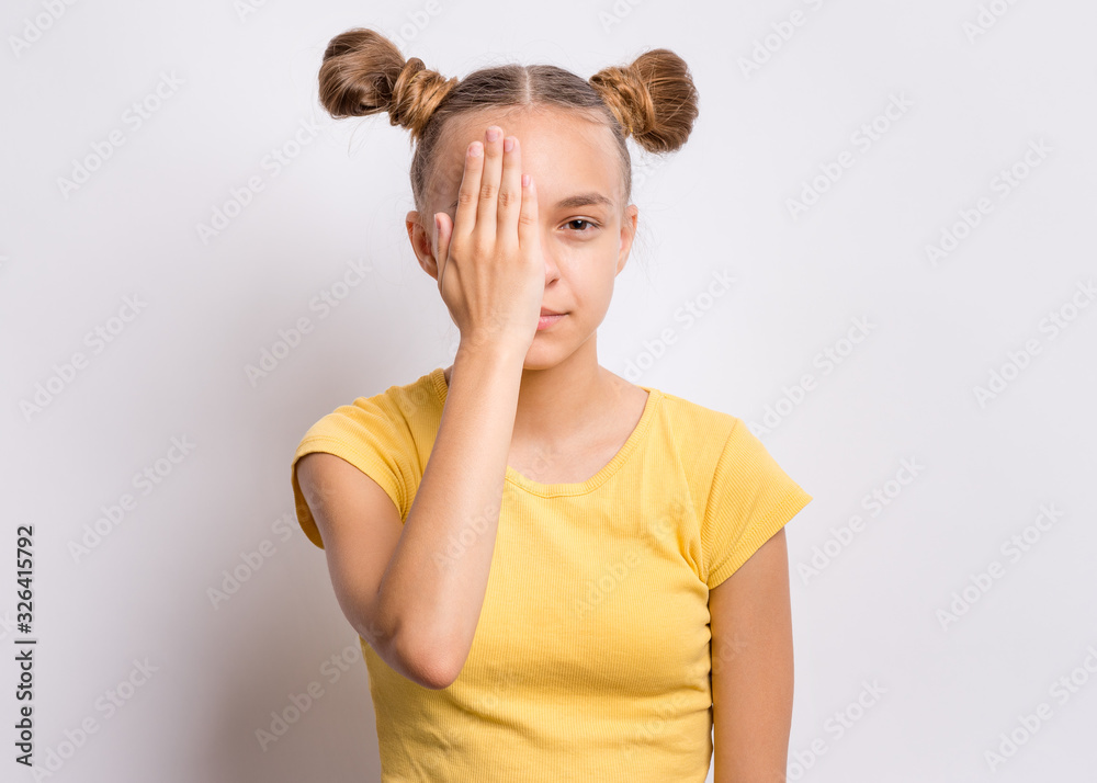 Portrait of teen girl covering one eye with hand checking eyesight. Human facial positive emotion. Smiling child on grey background. Health examinations. Teenager looking at camera. Portrait of teen girl covering one eye with hand checking eyesight. Human facial positive emotion. Smiling child on grey background. Health examinations. Teenager looking at camera.