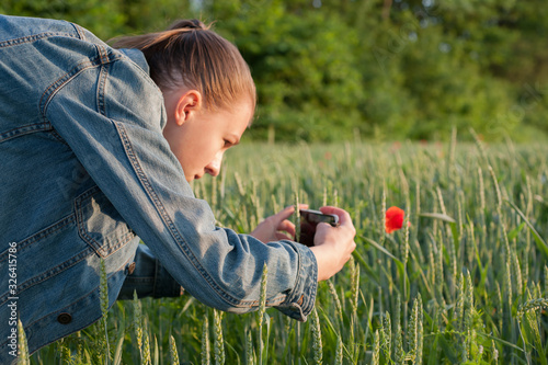 girl walking among green fields, collecting wildflowers takes beautiful photos on the phone