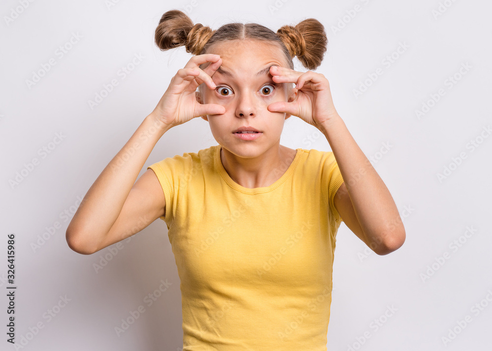 Silly teen girl making grimace - funny shocked face. Surprised child with big eyes, on grey background. Emotional portrait of amazed teenager looking at camera. Emotions and signs. Silly teen girl making grimace - funny shocked face. Surprised child with big eyes, on grey background. Emotional portrait of amazed teenager looking at camera. Emotions and signs.