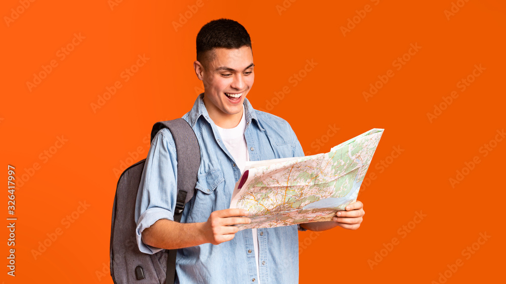 Happy traveler looking at city map over orange background Happy traveler looking at city map over orange background