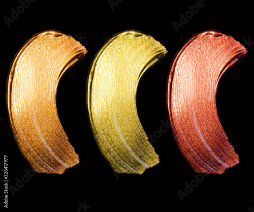 Creative brushstrokes of gold paint isolated on a black background. Gold paint texture.Acrylic gold paint. Smears of cosmetics, blush, highlighter, eye shadow, lipstick.