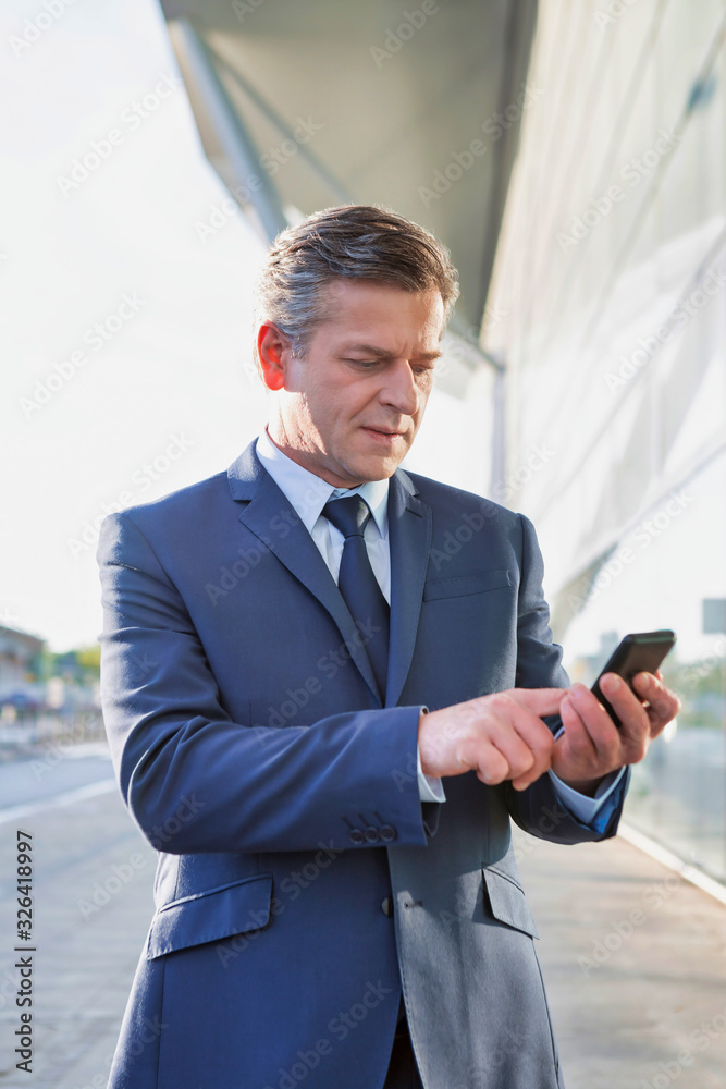 Portrait of mature attractive businessman using smartphone while standing in front of airport Portrait of mature attractive businessman using smartphone while standing in front of airport