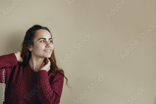 Happy young latin woman in claret sweater posing at beige background. Friendly looking. Copy space