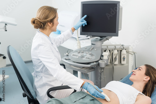 doctor making ultrasound scan of stomach to smiling patient and pointing at blank screen
