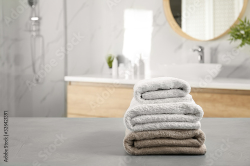 Stack of clean towels on grey stone table in bathroom. Space for text
