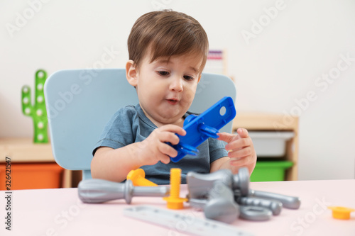 Little child playing with toy construction tools at table