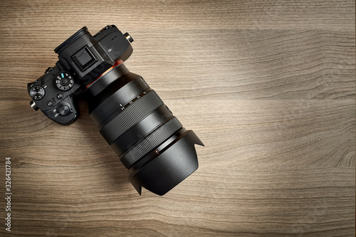 top view of a modern digital mirrorless full-frame camera with attached zoom lens and hood on wooden table