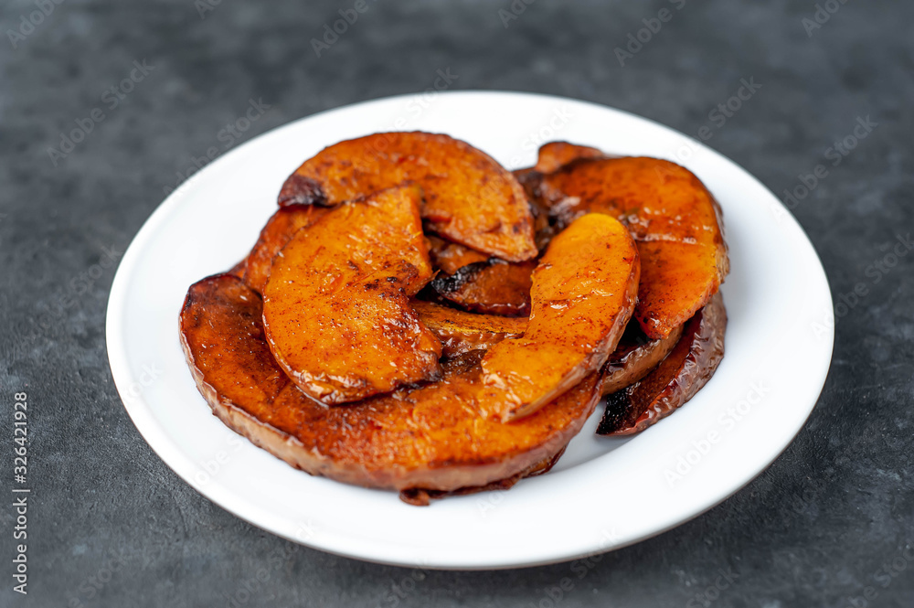 slices of fried pumpkin with spices on a white plate on a stone background