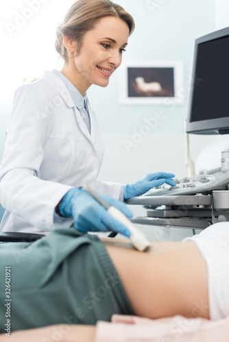 Fototapeta Naklejka Na Ścianę i Meble -  smiling female doctor examining stomach of patient with ultrasound scan in clinic