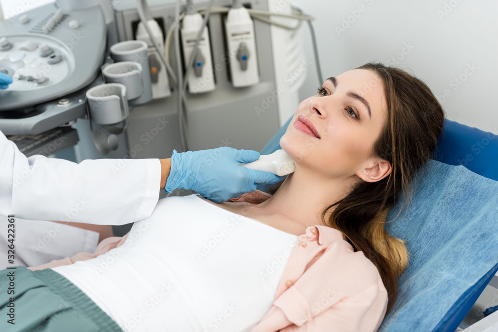 professional doctor examining thyroid of smiling patient with ultrasound scan in clinic professional doctor examining thyroid of smiling patient with ultrasound scan in clinic