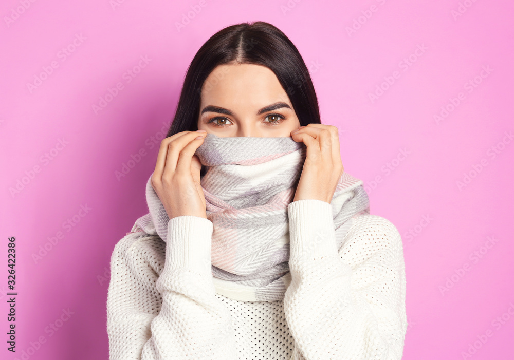 Young woman wearing warm sweater and scarf on pink background. Winter season Young woman wearing warm sweater and scarf on pink background. Winter season