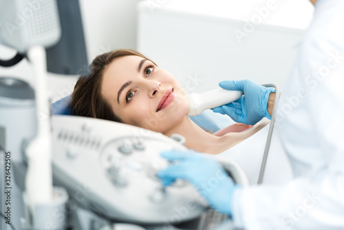 doctor examining thyroid of female patient with ultrasound scan in clinic