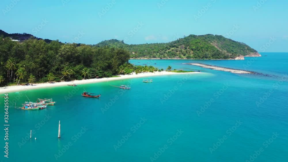 Tranquil bay with anchored boats floating on turquoise lagoon washing white sandy beach, palm trees on shoreline of tropical island, Thailand Tranquil bay with anchored boats floating on turquoise lagoon washing white sandy beach, palm trees on shoreline of tropical island, Thailand