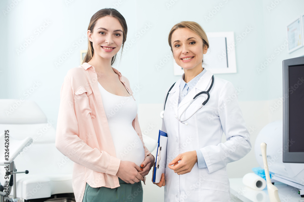 young pregnant woman standing with smiling gynecologist in clinic young pregnant woman standing with smiling gynecologist in clinic