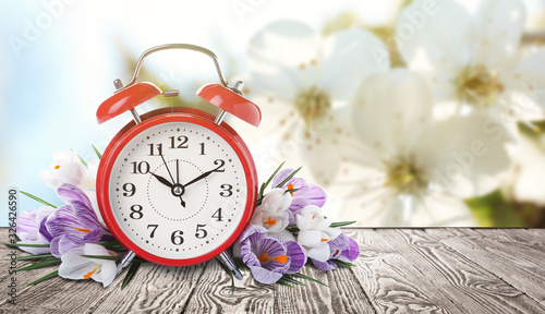 Red alarm clock and flowers on table against blurred background, space for text. Spring time