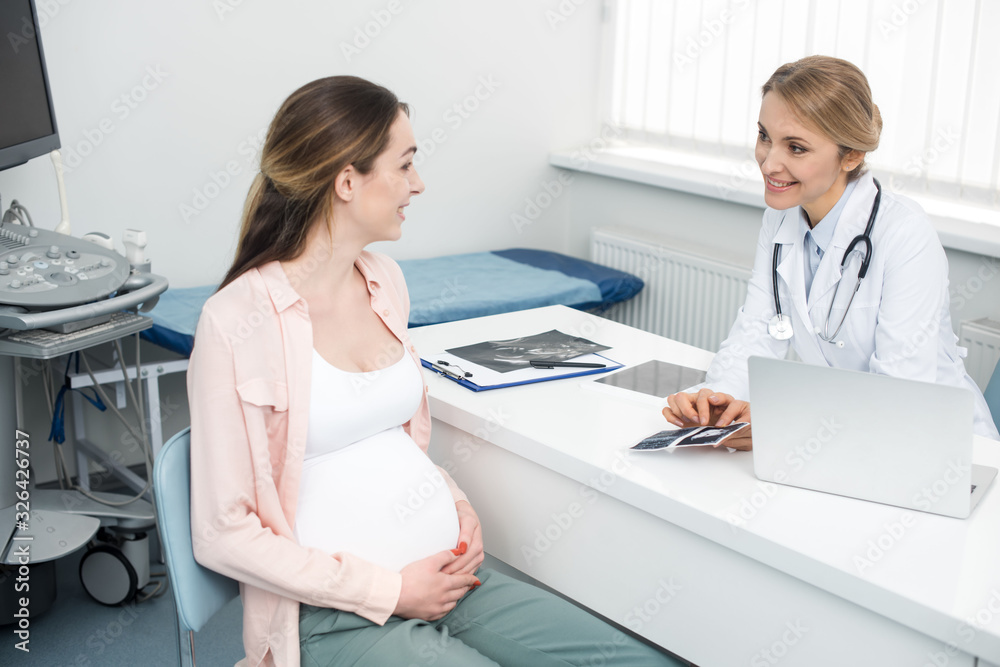 Obraz premium smiling doctor showing ultrasound scan to young pregnant woman in clinic