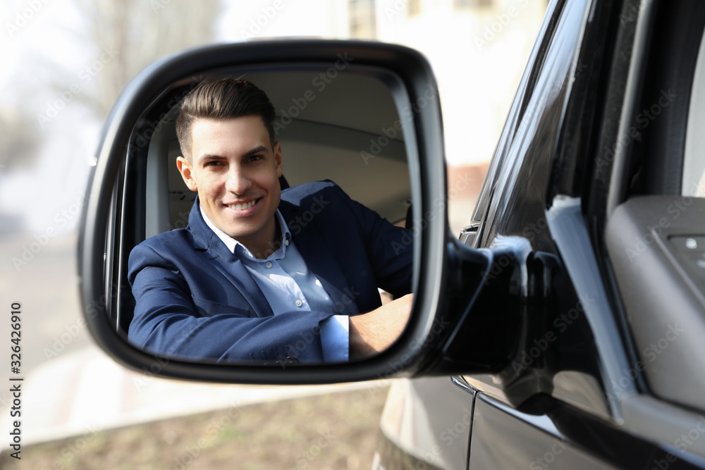 Handsome man looking into side view mirror of modern car outdoors Handsome man looking into side view mirror of modern car outdoors