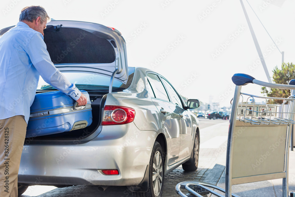 Fototapeta premium Portrait of mature businessman putting his luggage on car trunk with lens flare