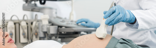 panoramic shot of professional doctor examining belly of pregnant woman with ultrasound scan photo