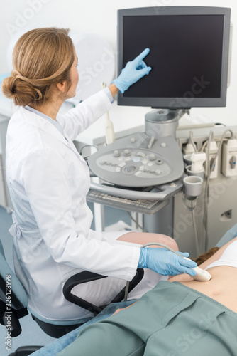 blonde doctor making ultrasound scan of stomach and pointing at blank screen