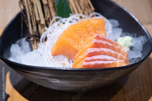 Salmon sashimi served on ice in black bowl