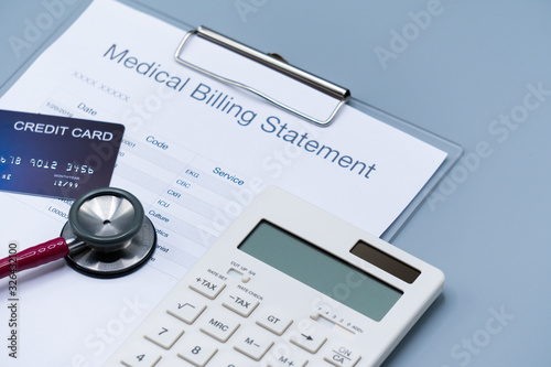 top view picture of medical billing statement, cradit card, white calculator and pink stethoscope on the gray background photo