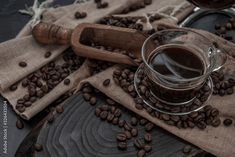 Cup of coffee and coffee beans roating with old wooden scoop and coffee beans around on the wooden and dark stone background. Close-up.