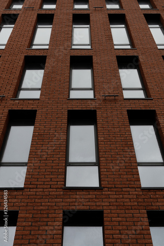 An orange brick office building. Facade with many windows. Angle view from below. Chicago style. New building for rent. Vertical photo.