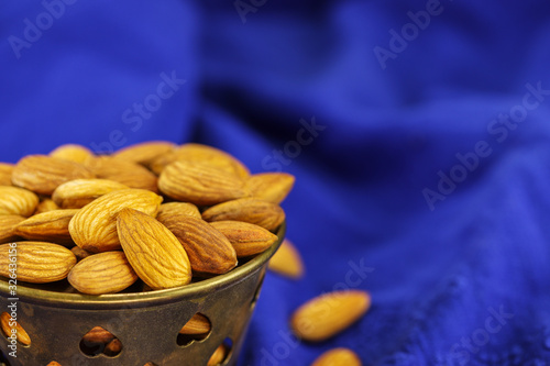 A metal bowl filled with almonds on a blue background