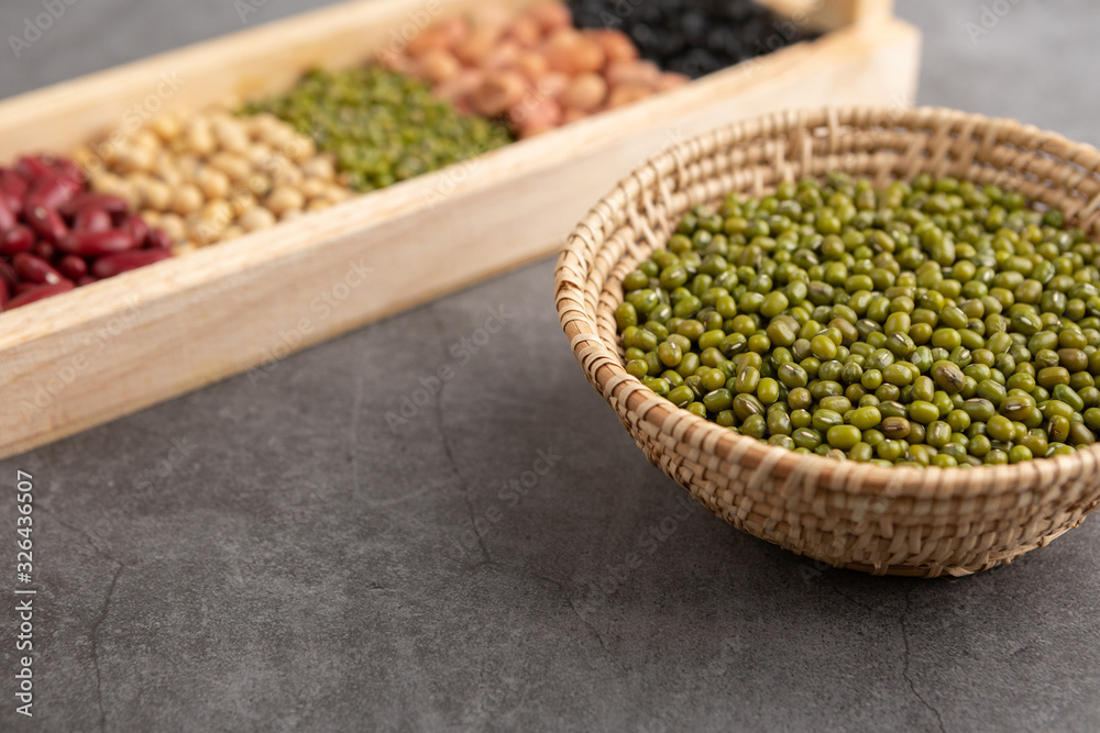 Green beans and grains in the wooden basket and in the wooden tray placed on the black cement floor. High angle view. Green beans and grains in the wooden basket and in the wooden tray placed on the black cement floor. High angle view.