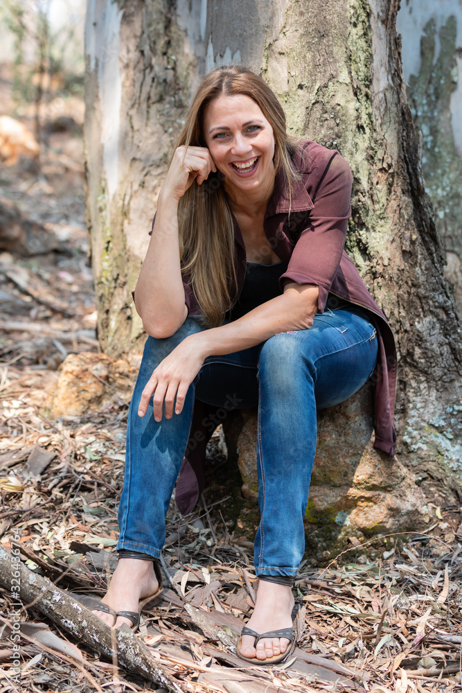 Portrait of a brunet woman with a blue denim and maroon jacket sitting against a tree Portrait of a brunet woman with a blue denim and maroon jacket sitting against a tree