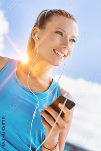 Portrait of young attractive woman standing while using and listening to music on her smartphone in park