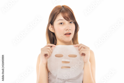 Young Asian girl with facial mask looking at camera over white background. Cosmetic procedure. Beauty spa and cosmetology.