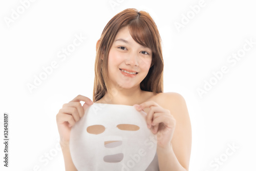 Young Asian girl with facial mask looking at camera over white background. Cosmetic procedure. Beauty spa and cosmetology.