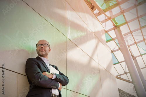 Portrait of businessman standing with arms crossed while leaning on wall photo