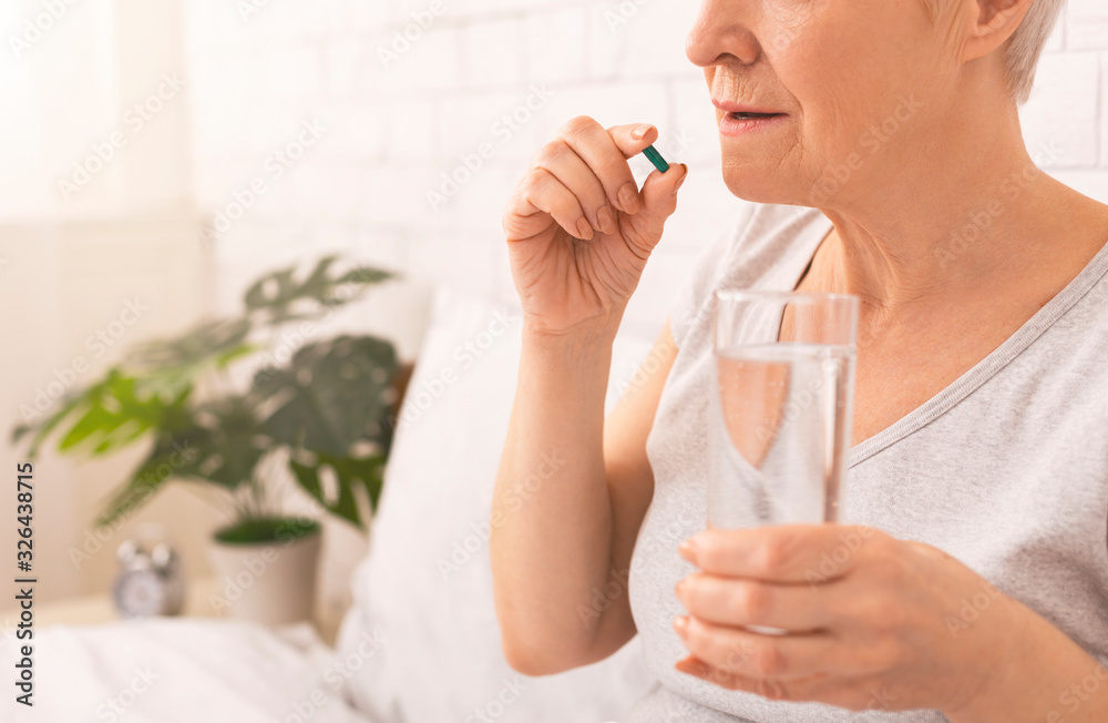 Healthy senior lady taking pills with glass of water in bed Healthy senior lady taking pills with glass of water in bed