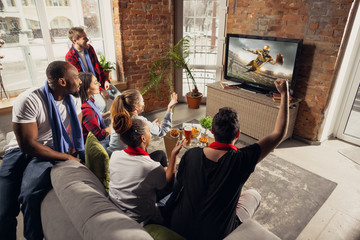Excited group of people watching american football, sport match at home. Multiethnic group of emotional friend, fans cheering for favourite national team, drinking beer. Concept of emotions, support.
