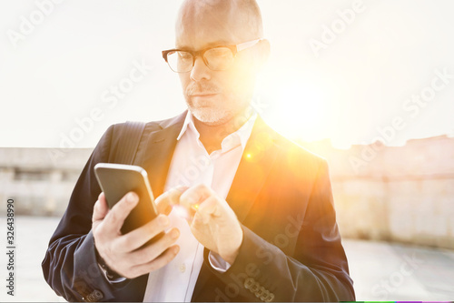 Portrait of businessman using smartphone while leaning on wall photo