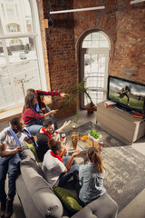 Excited group of people watching american football, sport match at home. Multiethnic group of emotional friend, fans cheering for favourite national team, drinking beer. Concept of emotions, support.