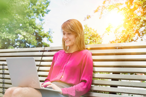 Portrait of young attractive businesswoman sitting on bench while working on her laptop