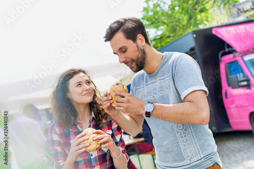 Young attractive couple eating hamburgers against food truck