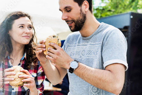 Young attractive couple eating hamburgers against food truck with lens flare in background