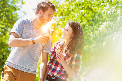 Portrait of young attractive couple walking while eating ice cream with lens flare in background