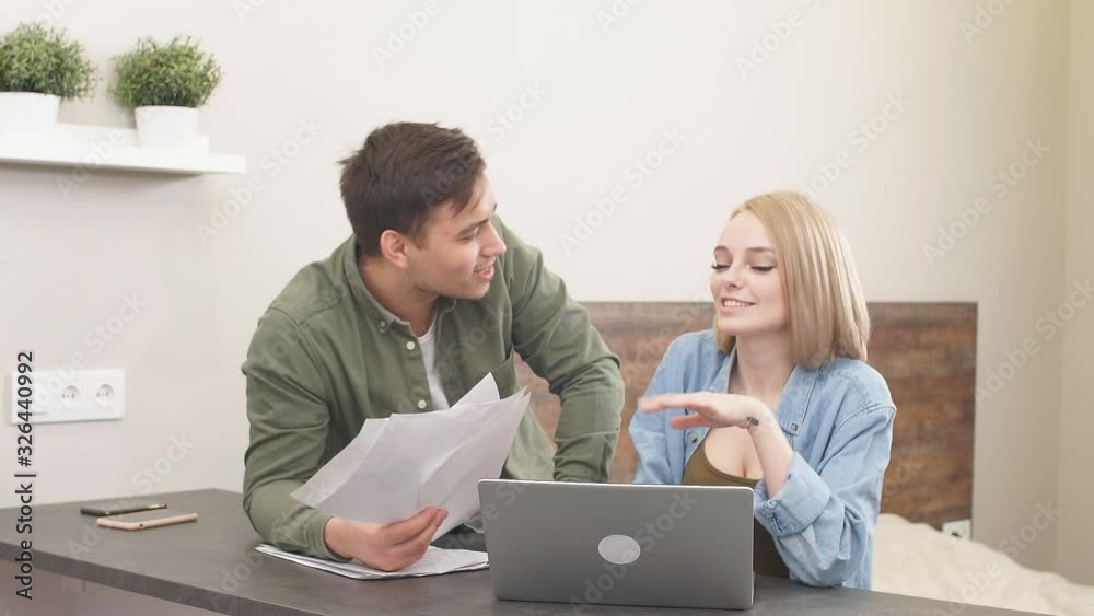 Happy married couple discuss financial issues of family, performing audit at home, caucasian man and woman sit together at table and smile while checking finance Happy married couple discuss financial issues of family, performing audit at home, caucasian man and woman sit together at table and smile while checking finance