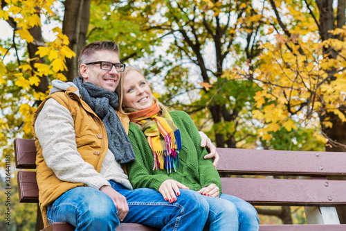 Portrait of mature couple sitting on bench while enjoying autumn in park © moodboard