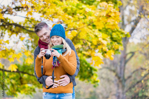 Portrait of mature beautiful woman showing pictures on camera while her husband is hugging her from behind in park
