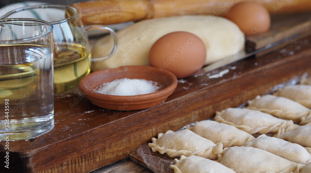 Wooden background with dumplings and dough ingredients for making dumplings. Food and cooking utensils on a brown kitchen board. Place for text. The concept of cooking dough.