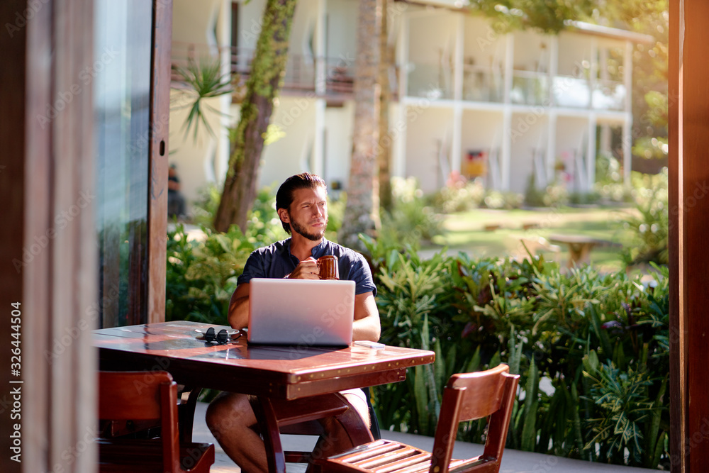 Freelance concept. Relaxed young bearded man working on laptop computer while sitting on terrace. Freelance concept. Relaxed young bearded man working on laptop computer while sitting on terrace.
